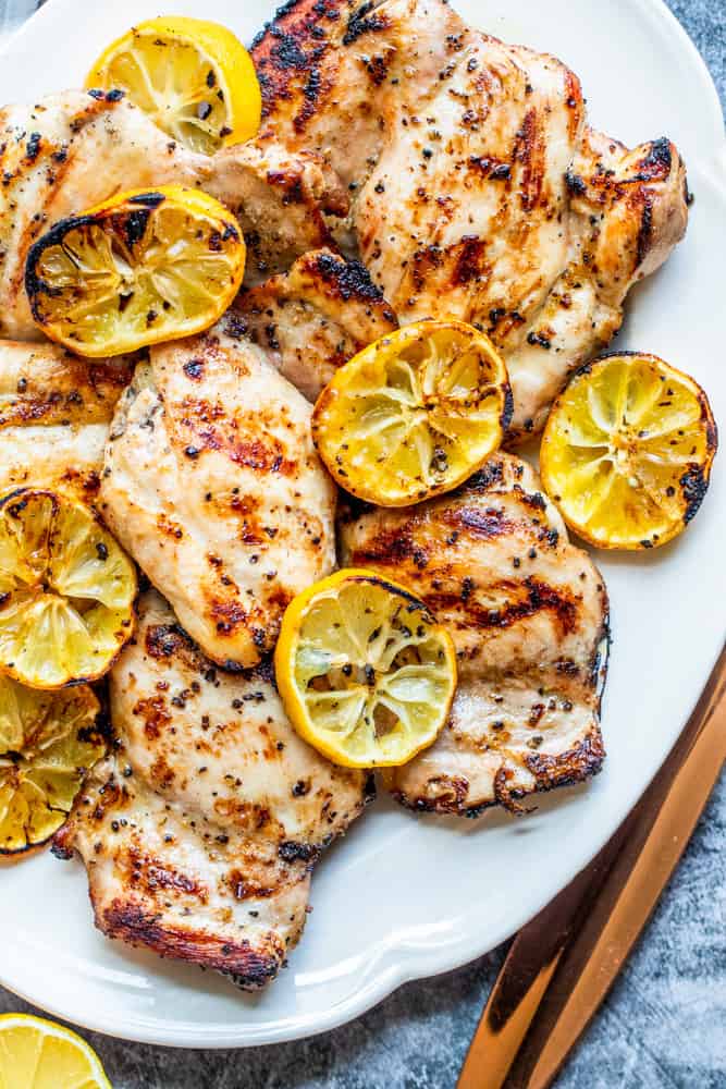 Overhead shot of grilled lemon pepper chicken on a white plate on a blue counter.