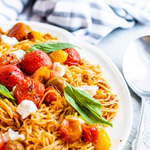 Pasta on a white dish on a white table with a silver spoon next to it.