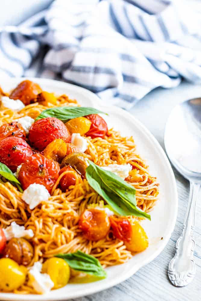 Red pesto pasta on a white serving platter with a silver spoon next to it.