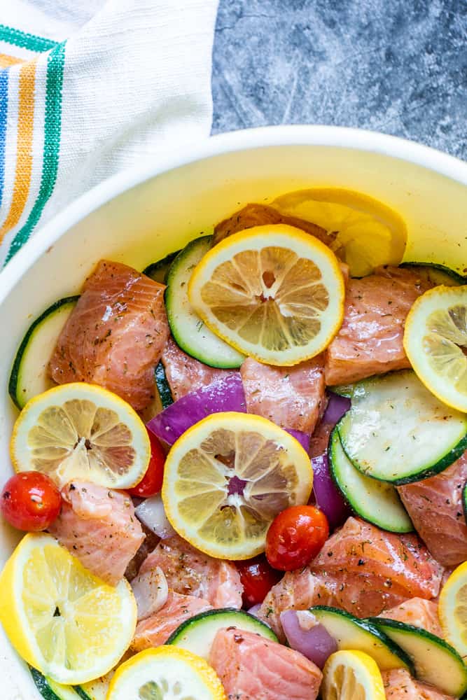 Salmon and cut veggies marinading in a large bowl on a blue counter.