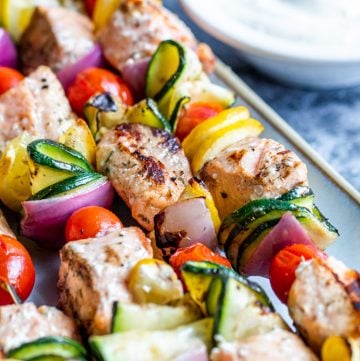 Cooked salmon kabobs on a gray plate on blue counter with sauce in background.