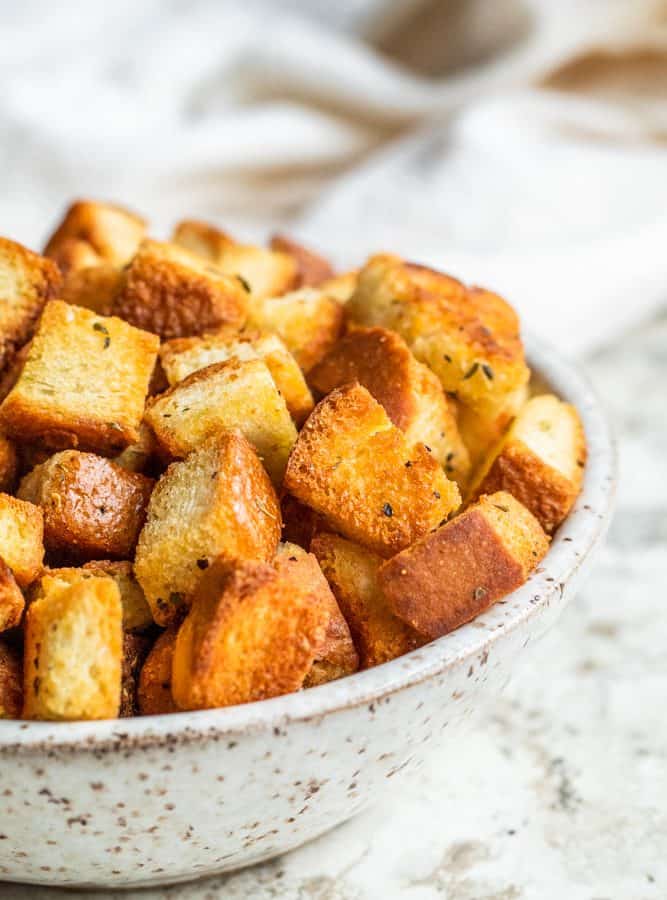 Croutons in a white bowl on a white counter.