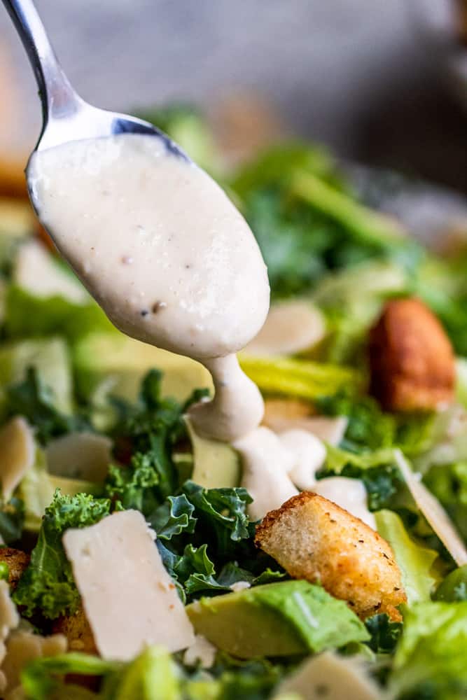 Silver spoon drizzling dressing over salad.