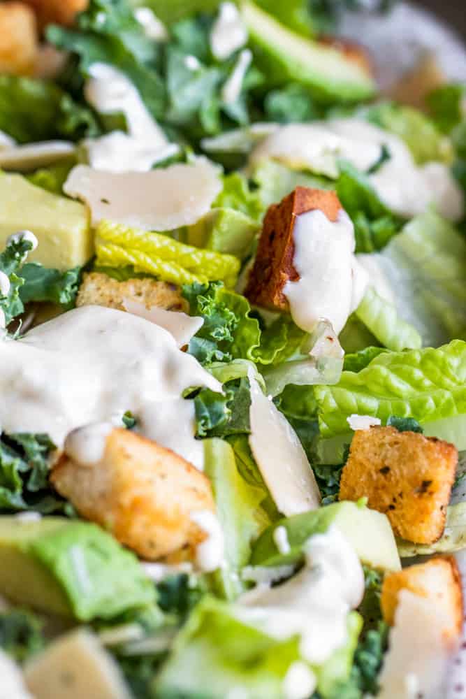 Close up shot of kale Caesar salad with dressing over the top.