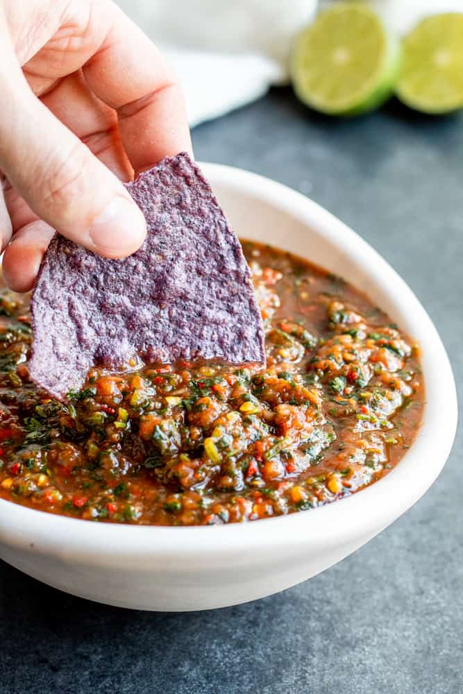 Hand dipping blue chip into a white bowl of red salsa.