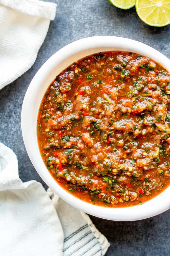 Overhead shot of salsa in a white bowl on a blue counter.