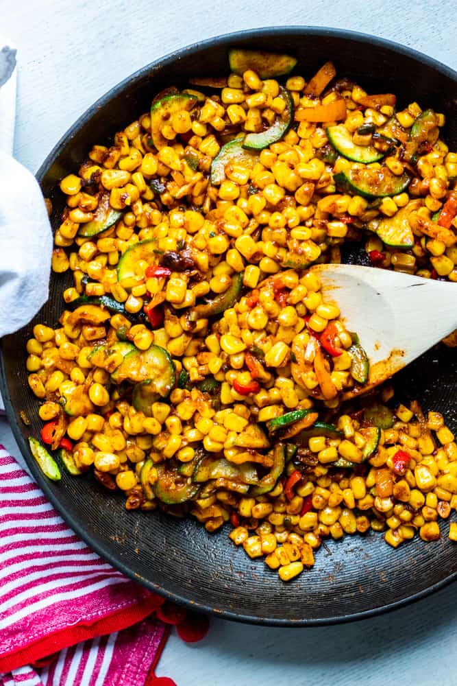 Black skillet filled with corn salad with a wooden spoon in it.