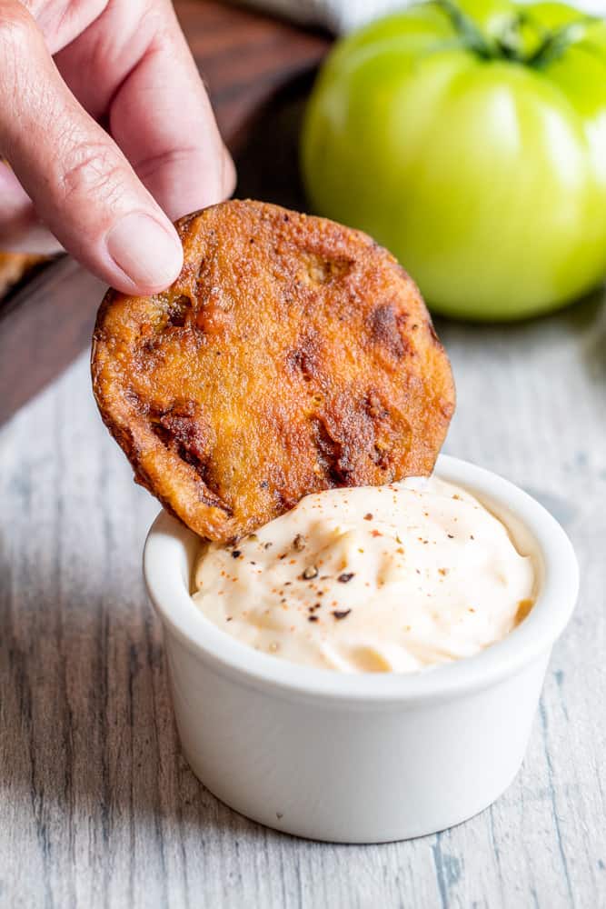 Hand dipping fried green tomato in a white bowl of hot mayo.