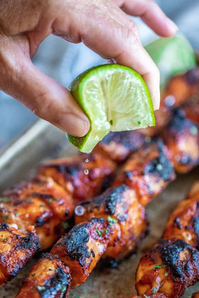 Hand holding lime slice and squeezing juice over chicken.