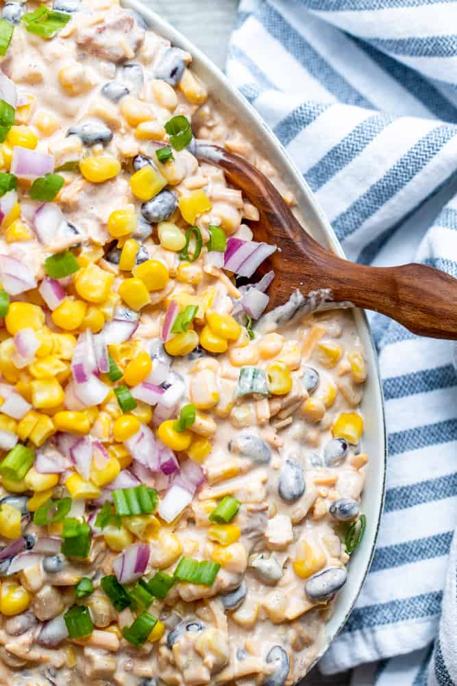 Wooden spoon scooping into large whit bowl of corn dip.