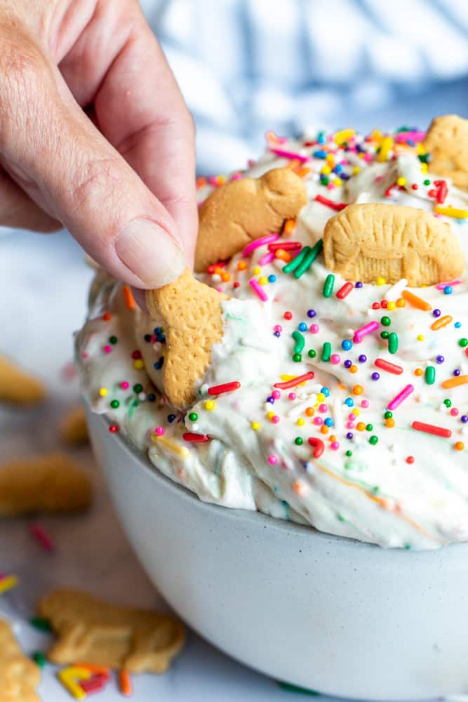 Hand dipping animal cracker in dunkaroo dip.