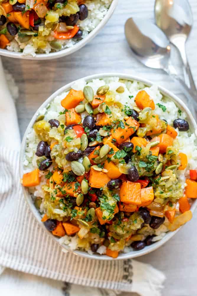 Overhead shot of two bowls of vegan burrito bowl on a white counter with two silver spoons.