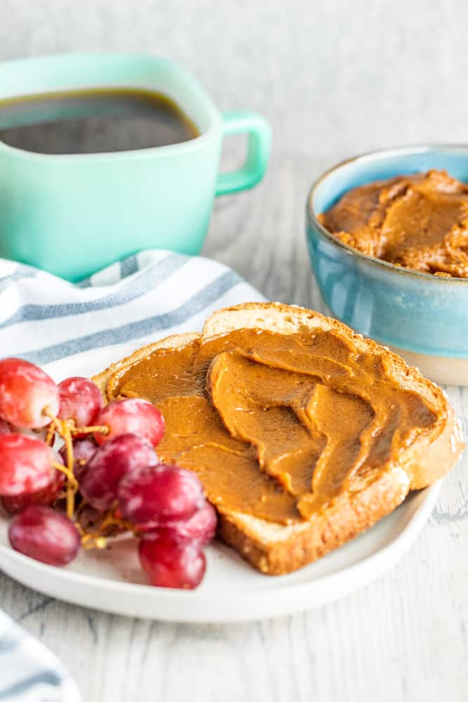 Cookie butter on toast on a white counter with coffee in background.