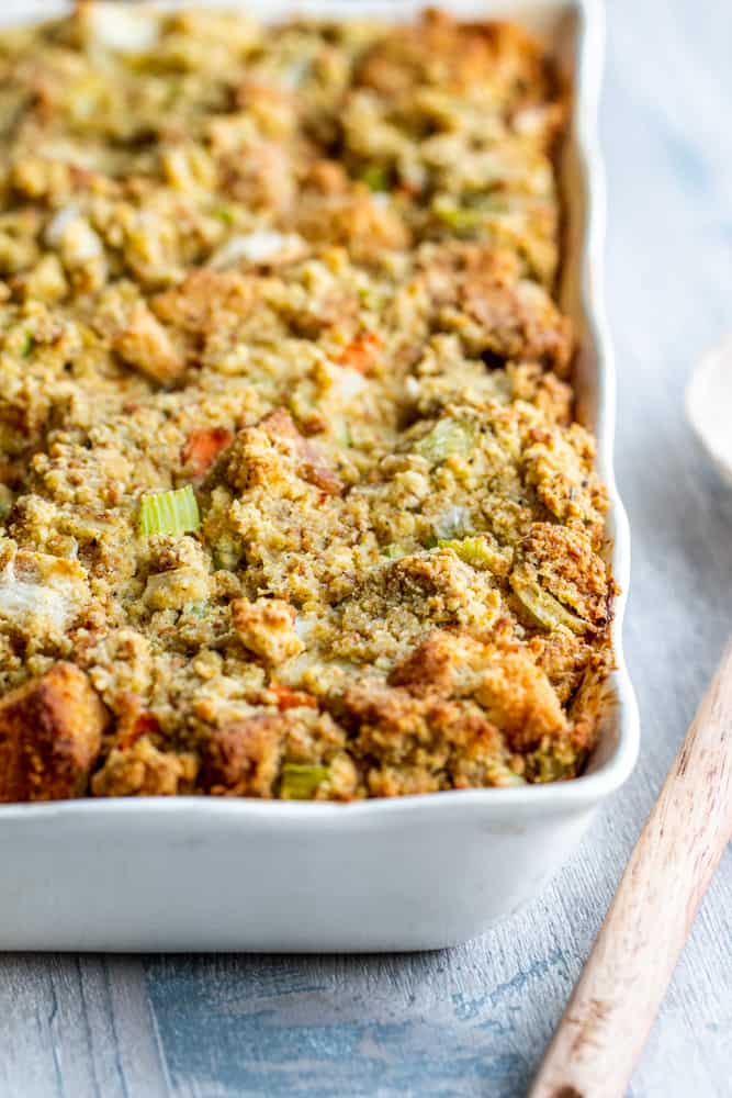 Cornbread dressing in a white baking dish with wooden spoon on the side.