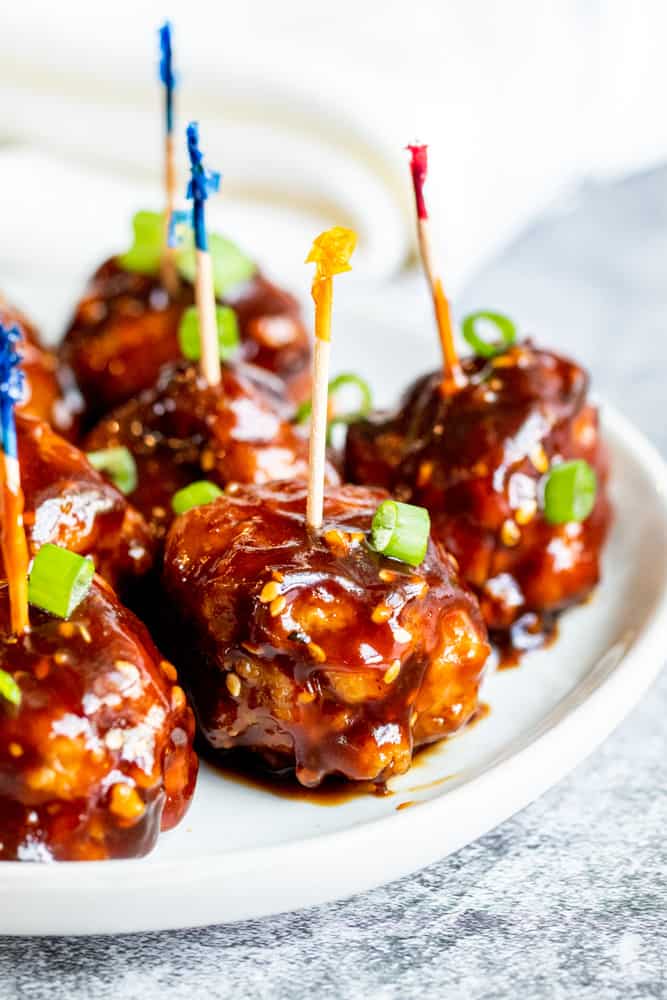 Meatballs on a white plate with toothpicks in them.