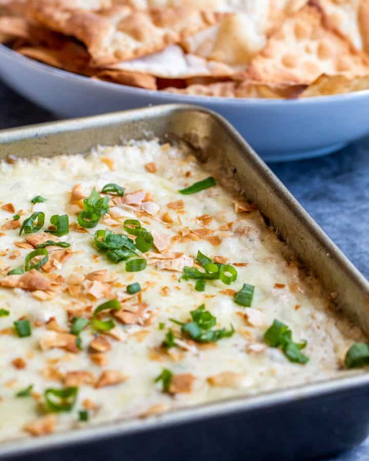 Crab dip in a baking pan on a blue counter with chips in the background.