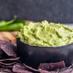Angle shot of creamy guacamole in a black bowl with chips.