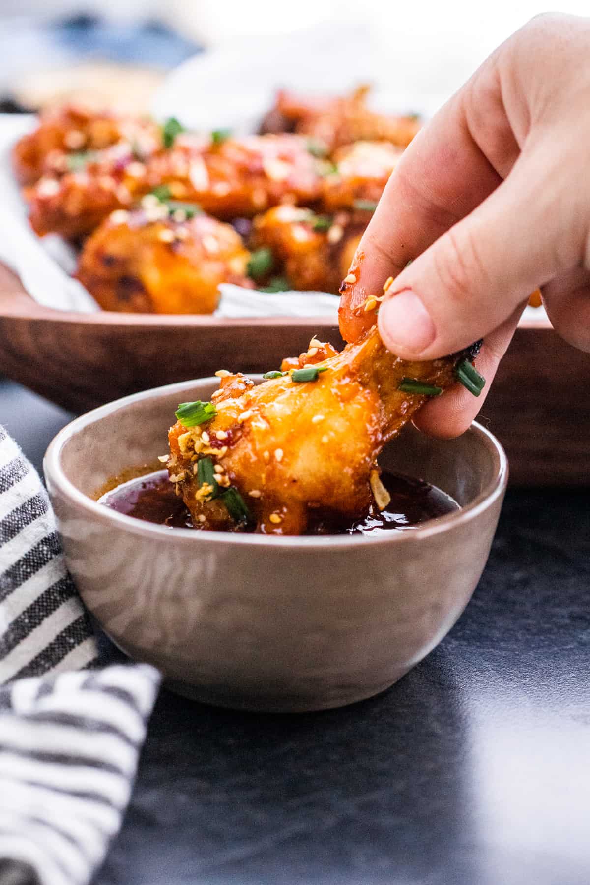 Hand dipping chicken wing into gray bowl filled with sauce.