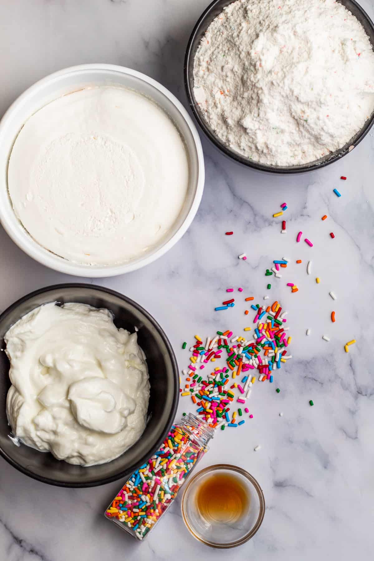 Overhead shot of ingredients laid out on a marble table for funfetti dip.