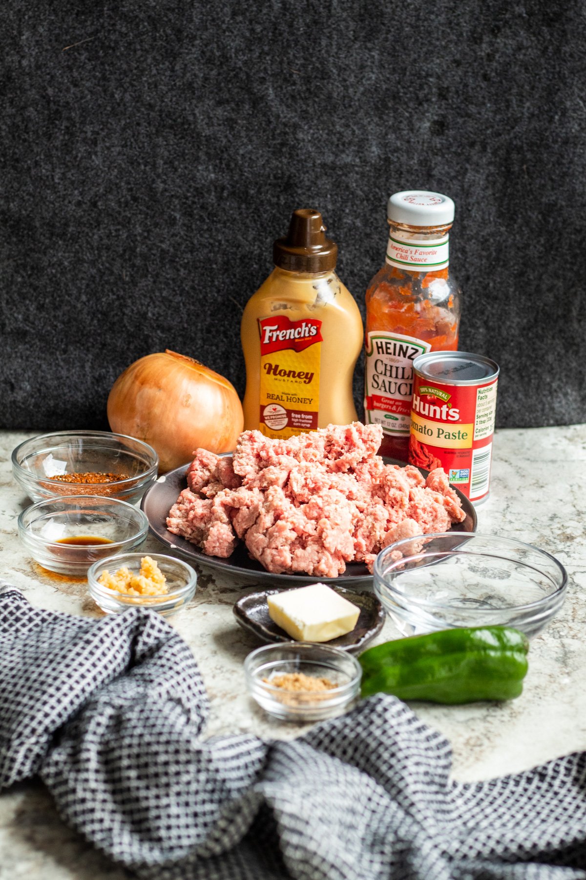 Sloppy joe ingredients on a white counter with gray background in jars and glass bowls.