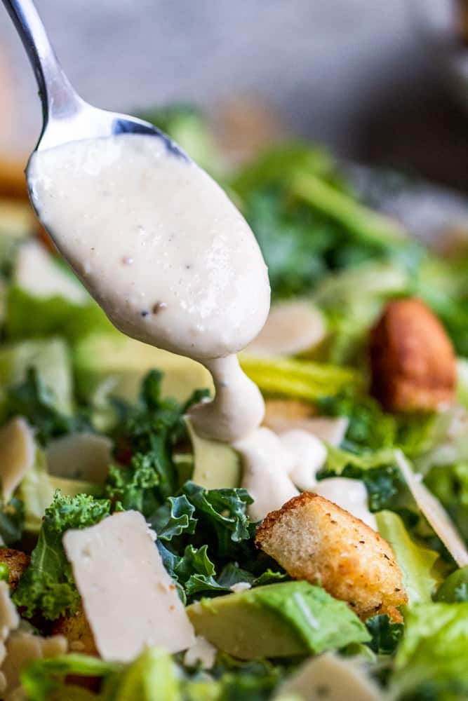 Silver spoon dripping dressing on salad.