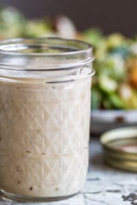 Caesar dressing in mason jar with salad in the background.