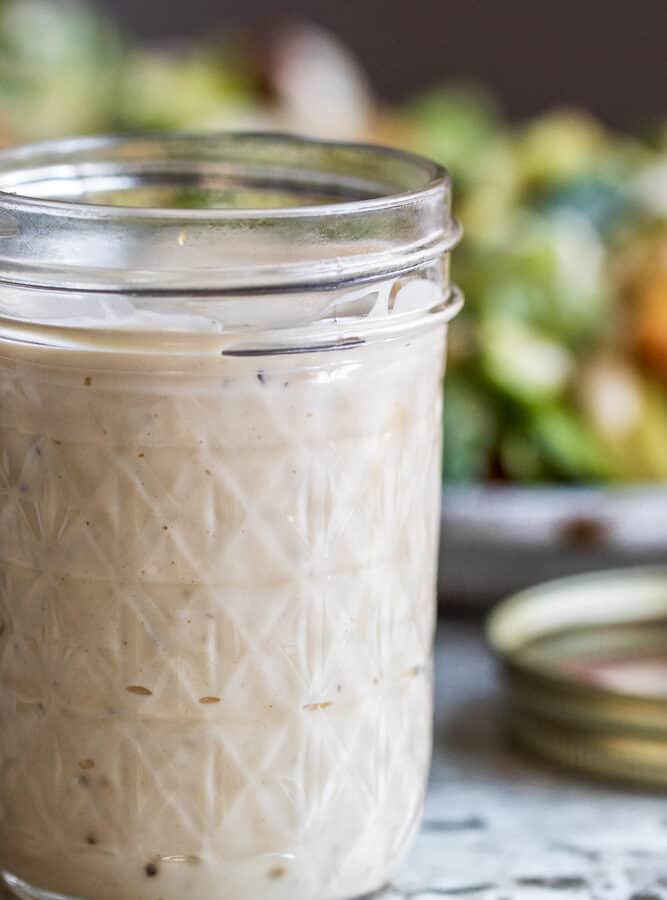 Caesar dressing in mason jar with salad in the background.