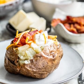 Baked potato on gray plate loaded with toppings.