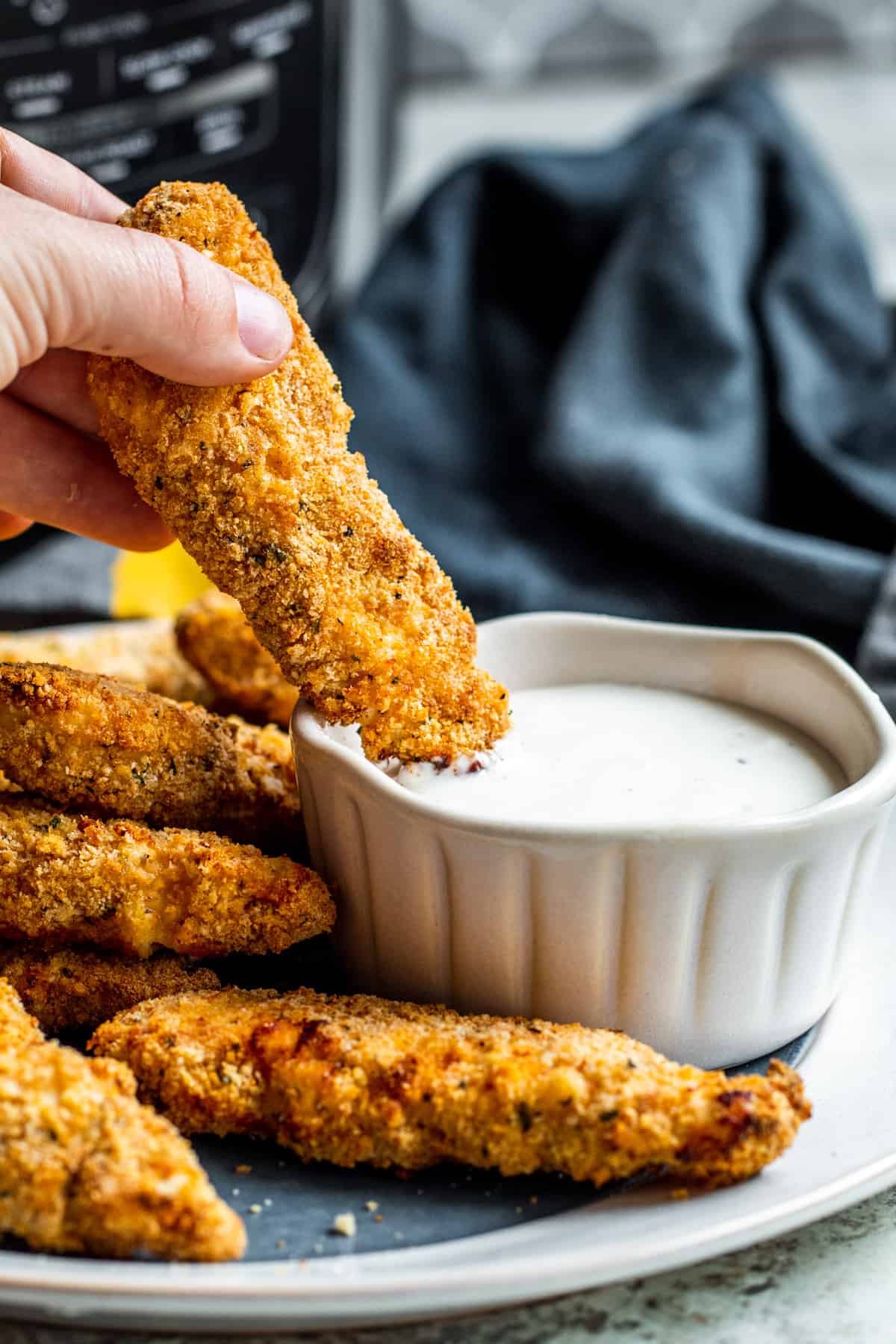 Hand dipping chicken tender in white bowl of ranch.