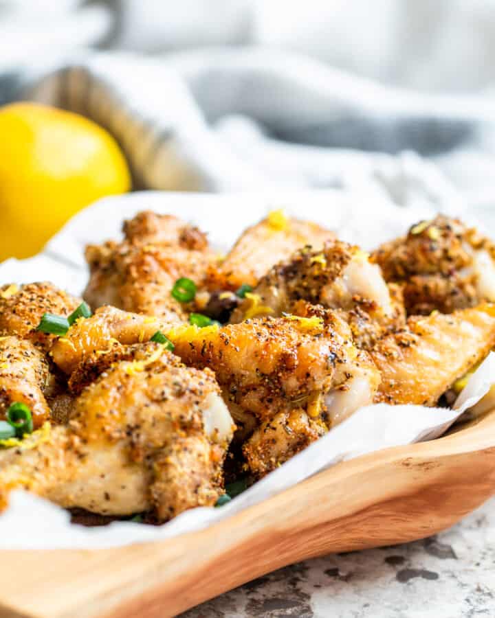 Wooden bowl filled with lemon pepper wings on white counter.