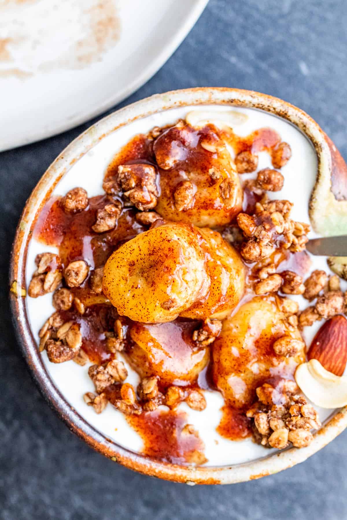 Overhead shot of bananas on top of granola and yogurt in small tan bowl.