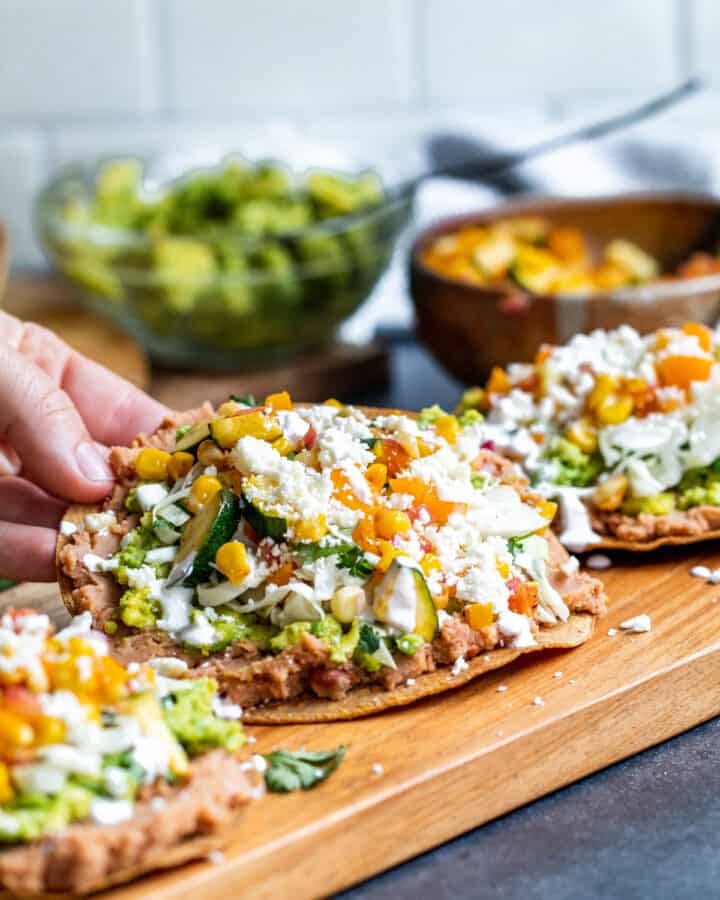 Hand picking up tostada off of cutting board.