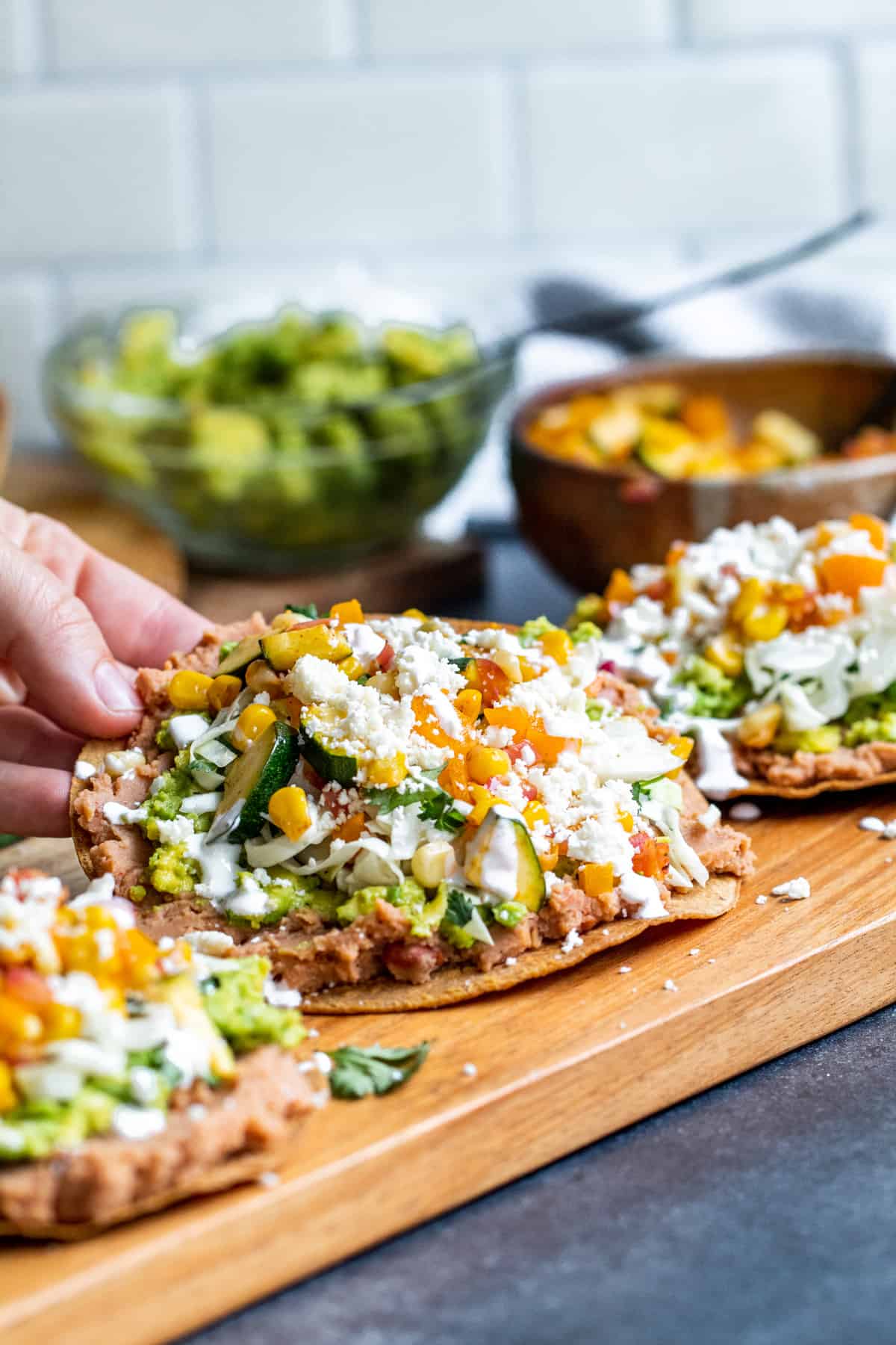 Hand picking up tostada off of cutting board.