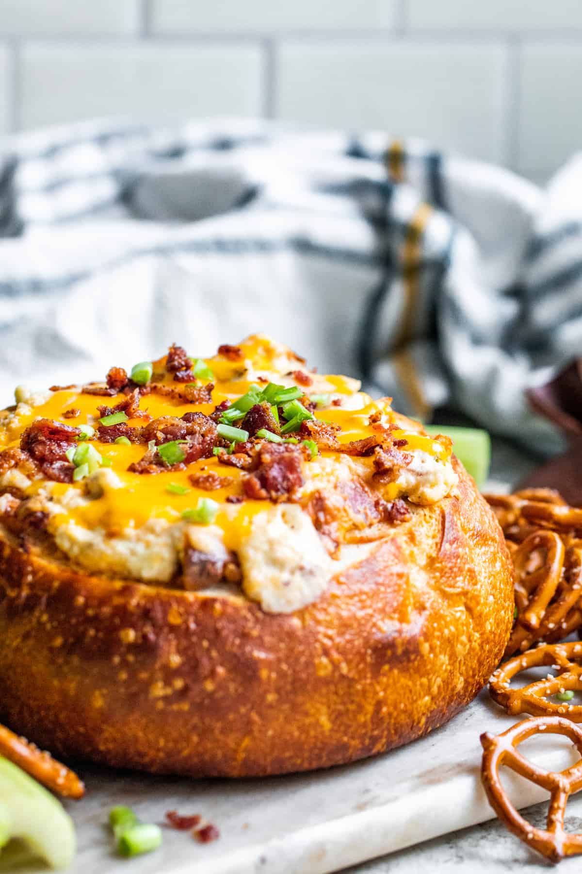 Bacon cheese dip in a bread bowl with dippers on a white counter.