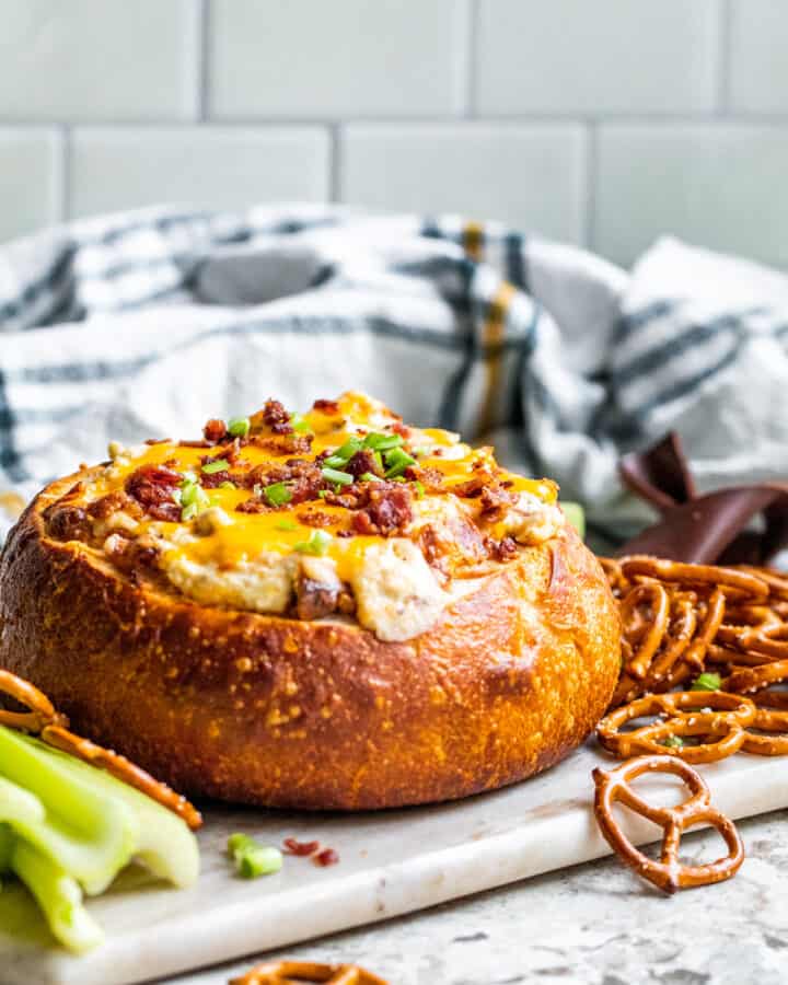 Baked dip in a bread bowl on white counter sitting on serving tray.