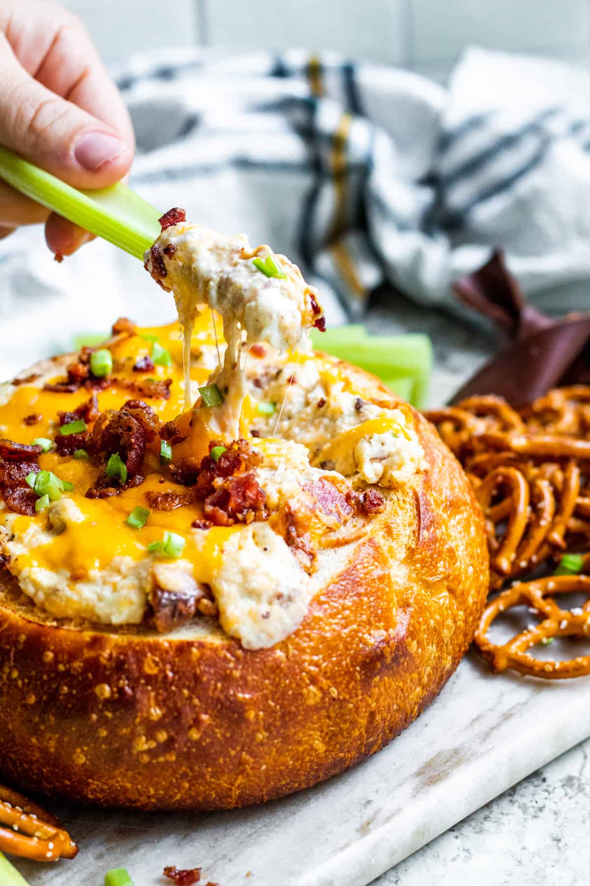 Celery being dipped into bacon dip in bread bowl.