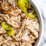 Overhead shot of cooked crockpot chicken in a large white bowl shredded.