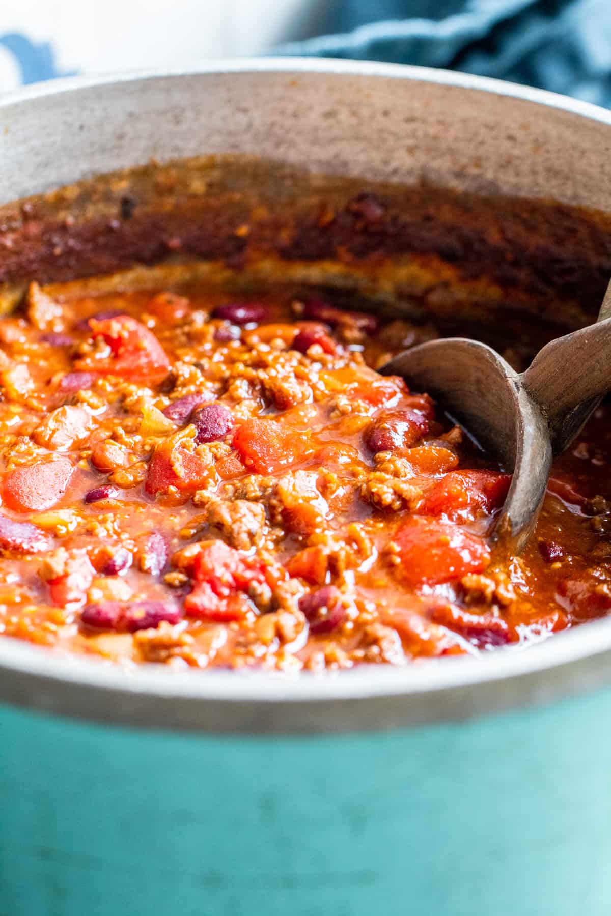 Blue pot filled with chili with wooden spoon sitting in it.