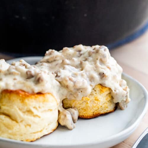 Biscuits on white plate topped with sausage gravy.